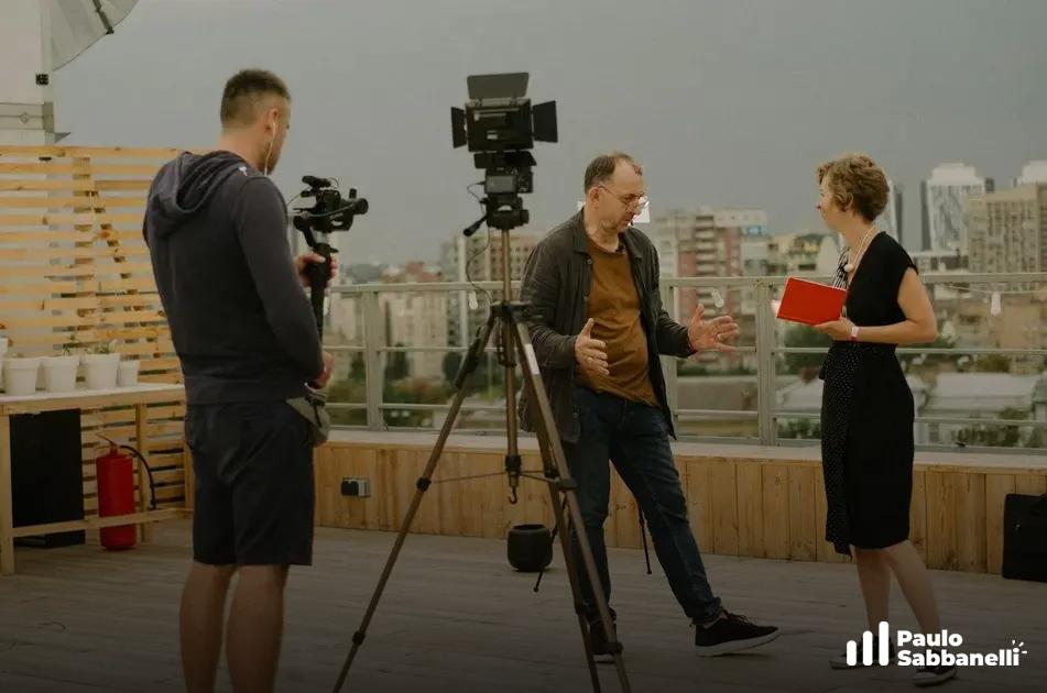 Equipe de filmagem grava homem falando em terraço com vista para a cidade ao fundo