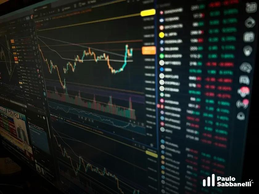 Tela escura de monitor exibe gráfico de candles e lista de ativos financeiros em cores variadas