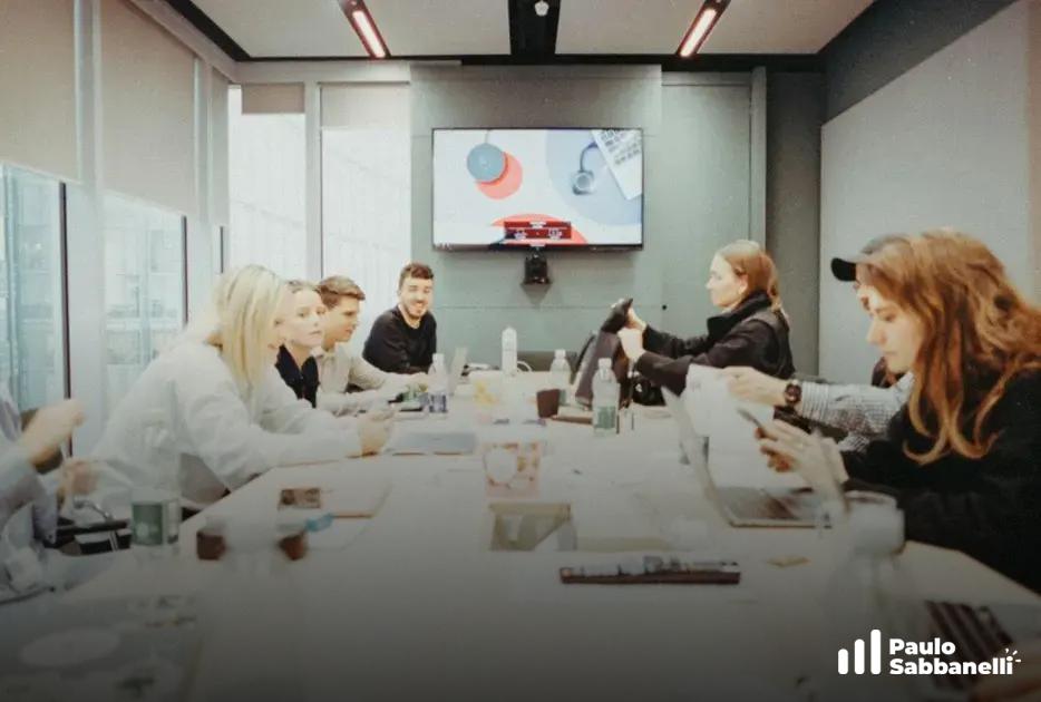 Reunião de equipe em sala de vidro com tela exibindo ícones coloridos ao fundo