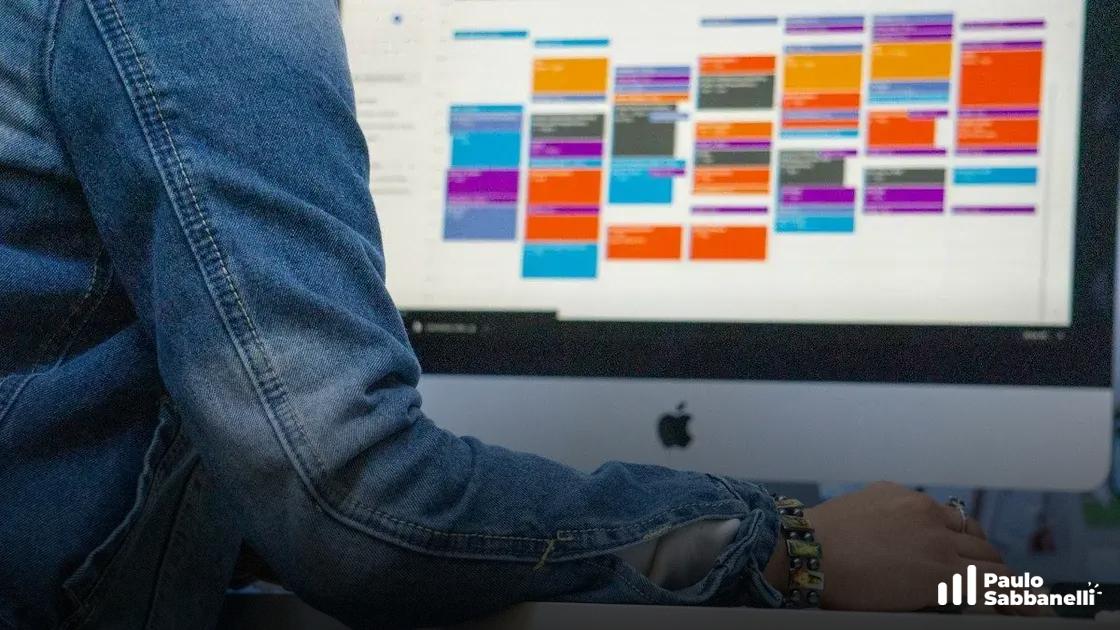 Pessoa de jaqueta jeans digitando em um iMac com um calendário colorido na tela