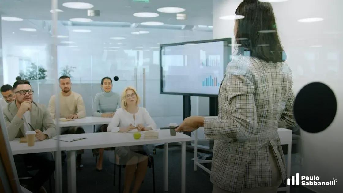 Mulher apresenta gráfico de barras em tela para colegas sentados em sala de reunião envidraçada