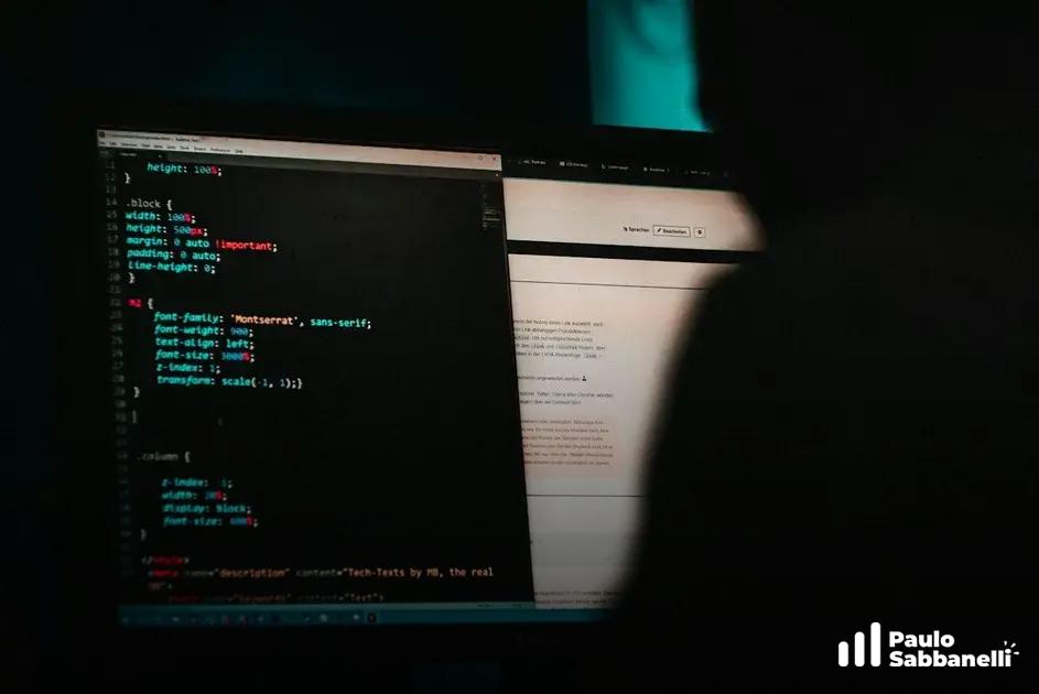 Silhueta de uma pessoa em frente a dois monitores, um com código CSS e outro com uma página clara