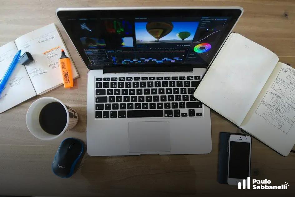 Vista superior de mesa com notebook aberto em editor de vídeo, caderno, café e celular