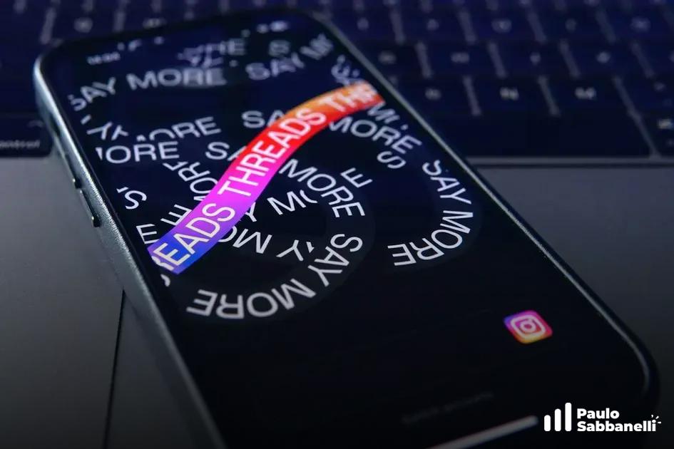 Celular apoiado em teclado exibindo a tela de abertura do aplicativo Threads com efeito espiral